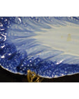 Close-up of blue and white porcelain dish with hand-painted design and textured, leaf-like edge.