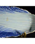 Close-up of blue and white porcelain dish with hand-painted leaf pattern and scalloped edge, displayed on a stand.