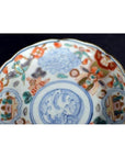 Close-up of vintage Chinese porcelain plate with blue, orange, and green hand painted patterns on dark background.