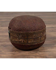 Brown rattan hat box with weathered patina on a wooden floor.