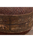 Close-up of a brown rattan circular hat box with weathered patina and faded floral patterns.