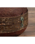 Close-up of a brown rattan circular hat box with weathered patina on a wooden floor.