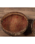 Brown rattan circular hat box with weathered patina on rustic wooden floor.