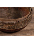 Brown rattan circular hat box close-up with weathered patina, shown on a wooden floor.