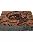 Close-up of vintage copper Batek ink block stamp with carved designs and Cyrillic text, used for printing or stamping.