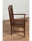 Brown wood Dutch Colonial armchair with pierced slats and bonnet rail, placed against a white brick wall indoors.
