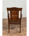 Brown wooden Dutch Colonial armchair with pierced slats and bonnet-style rail on a wooden floor indoors.