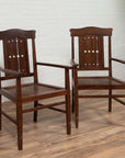 Brown wood Dutch Colonial armchairs with pierced slats and bonnet rails on a wooden floor indoors.