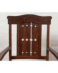 Close-up of brown wood Dutch Colonial armchair with pierced slats and bonnet rail, indoors by white brick wall.