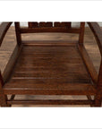 Brown wooden Dutch Colonial armchair with pierced slats and bonnet-style rail on wooden floor indoors.