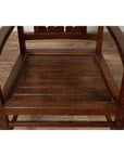 Brown wooden Dutch Colonial armchair with pierced slats and bonnet-style rail on wooden floor indoors.