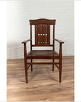 Brown wooden Dutch Colonial armchair with pierced slats, on wood floor next to a white brick wall indoors.
