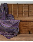 Purple silk embroidered fabric with silver and gold accents draped over an open wooden chest.