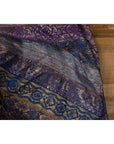 Close-up of purple silk fabric with purple, silver, and gold embroidery on a wooden surface.