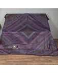 Purple silk embroidered fabric with silver and gold accents draped on a stand indoors.