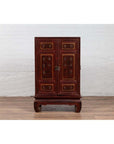 Red lacquered wood display cabinet with gold calligraphy on a wooden floor indoors.