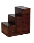 Brown wood staircase tansu cabinet with four drawers and metal handles, Japanese style, indoors.