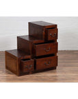 Brown wood Javanese staircase tansu cabinet with four drawers on wooden floor against a white brick wall indoors.