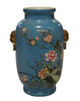 Close-up of vintage porcelain vase with hand painted flowers, birds, gold lion head handles, and glossy finish.