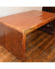 Large wood Waterfall Table with rectangular top on wooden floor beside white brick wall, wide angle view.