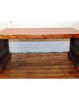 Light wood waterfall table with rounded edges on wooden floor, set against a white brick wall background.
