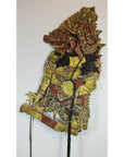Brown cowhide Wayang Kulit Balinese shadow puppet with ornate costume, large headdress, bold facial features, plain backdrop.
