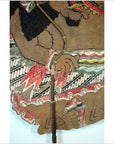 Close-up of painted Balinese cowhide Wayang Kulit shadow puppet with intricate patterns, hand holding wooden stick.