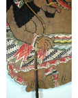 Close-up of painted Balinese cowhide Wayang Kulit shadow puppet with intricate patterns, hand holding wooden stick.
