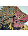 Close-up of a pink-faced Wayang Kulit shadow puppet made from Balinese cowhide, with large eyes and ornate headdress.