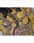 Close-up of gold-painted cowhide Wayang Kulit Balinese shadow puppet with detailed floral and intricate patterns.