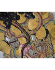 Close-up of gold-painted cowhide Wayang Kulit Balinese shadow puppet with detailed floral and intricate patterns.