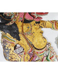 Close-up of gold, pink, and green Wayang Kulit shadow puppet made from Balinese cowhide on white background.