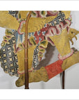 Close-up of gold, red, and blue Wayang Kulit Balinese shadow puppet made from cowhide on a white background.