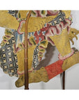 Close-up of gold, red, and blue Wayang Kulit Balinese shadow puppet made from cowhide on a white background.