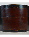 Close-up of round vintage hat box in dark wood with a central red rectangular panel, isolated on white background.