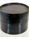 Close-up of a round dark wood hat box with fitted lid and visible grain, shown on a white surface.