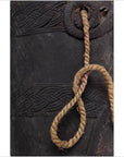 Close-up of a braided rope looped through a decorative brown wooden Indian pitcher on a plain background.