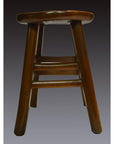 Brown wooden antique Indonesian stool with four legs and two footrests, set against a subtle gradient background.
