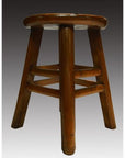 Brown wooden antique Indonesian stool with four legs and round seat on a gradient gray background.