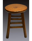 Brown wooden three-legged Indonesian stool with a round top and sturdy horizontal support bars, close-up view.