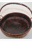 Dark brown woven bamboo offering basket with sturdy handle, close-up against a plain light background.
