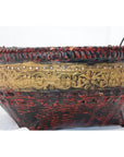 Close-up of red and gold woven bamboo offering basket with gilt décor, woven rim, and handles.