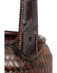 Close-up of natural woven basket with long wooden handle, metal plate, and keyhole detail.