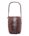 Close-up of a tall, dark brown woven basket with a rounded body and curved long handle, Thai-made.