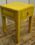 Yellow wood side table with horse hoof feet, single drawer, metal ring handle, and square legs, close-up view.