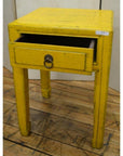 Yellow wood side table with a single drawer and horse hoof feet on a wooden floor.