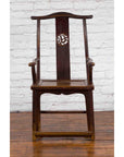 Brown wood Qing Dynasty scholar's armchair with carved splat beside a Chinese trunk on wooden floor.
