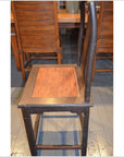 Dark brown wood Yoke Back Chair with high back and burl wood seat on wooden floor near matching table and chairs.