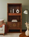 Antique elmwood bookcase with two shelves and drawers next to beige armchair with rust-colored throw.