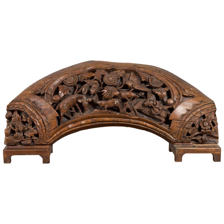 Brown wood arch sculpture with hand-carved animal and floral motifs on a dark antique chest.